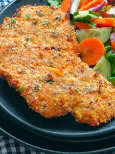 Panko crusted chicken with vegetable salad on a black plate.