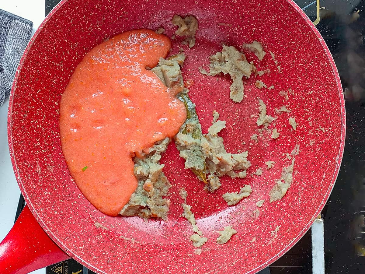 Tomato puree with sauteed onion paste in a pink wok pan.