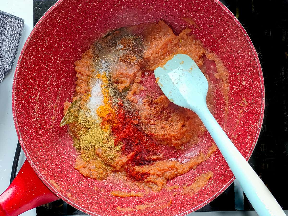 Spices with tomato puree and sauteed onion paste in a pink wok pan.