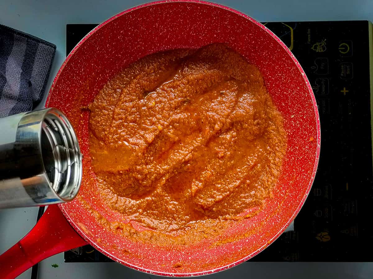 Water being added to the gravy for egg curry in a pink wok pan.