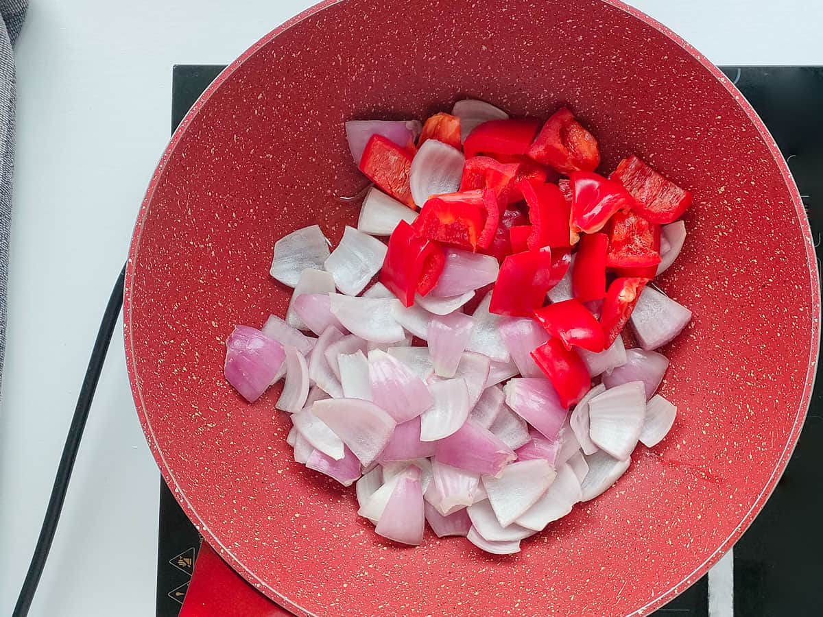 Diced onions and bell peppers in a pink wok pan.