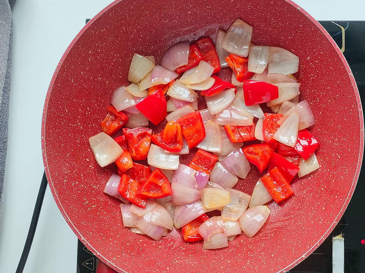 Sauteed onions and bell peppers in a pink wok pan.