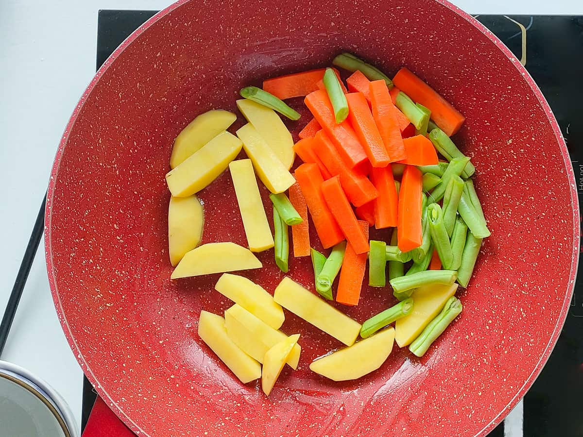 Sauteed carrots, potatoes and beans in a pink wok pan.