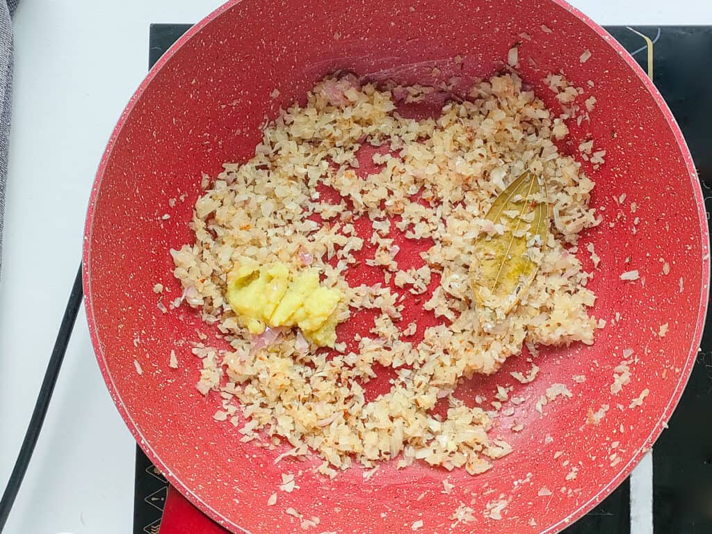 Browned onions and ginger garlic paste in a pink wok pan.