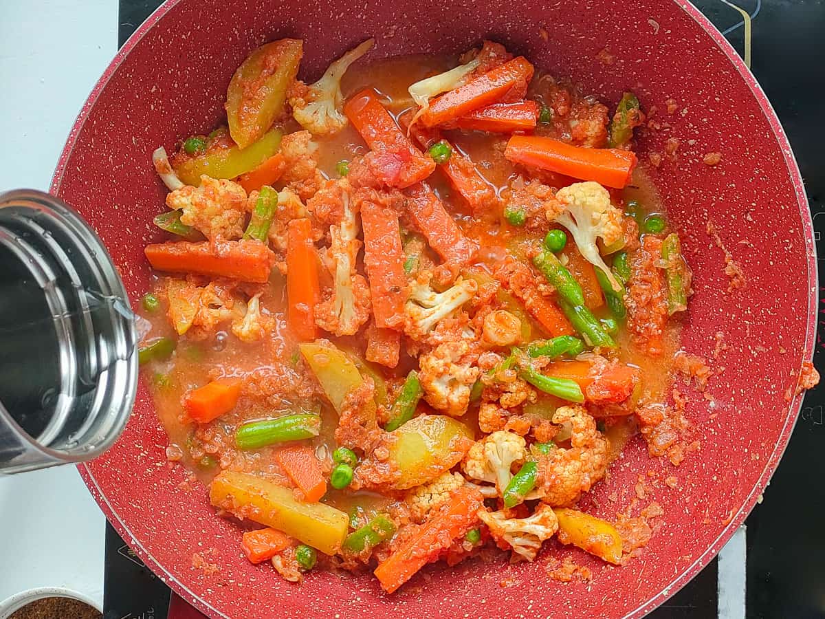 Water added to vegetables, spices and tomato gravy in a pink wok pan.