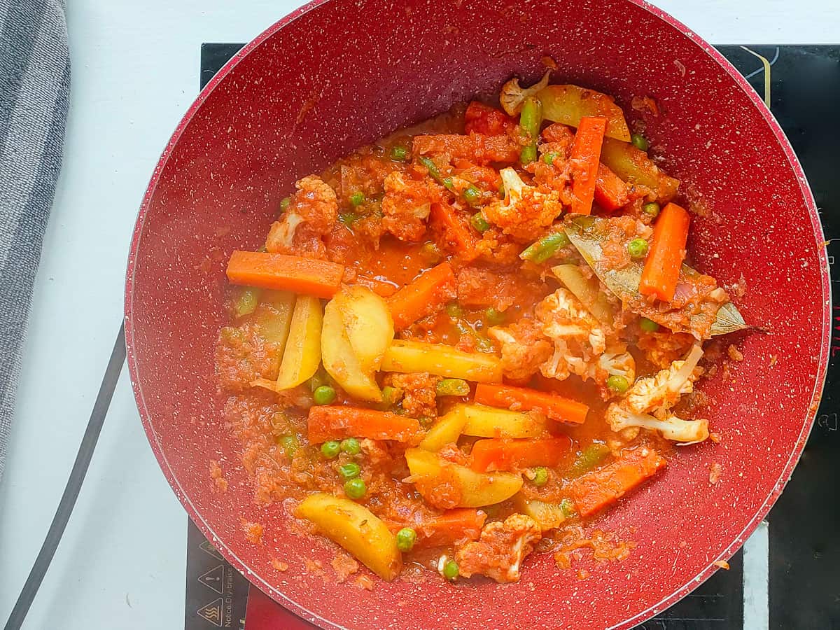 Mixed vegetables and spices in tomato gravy in a pink wok pan.