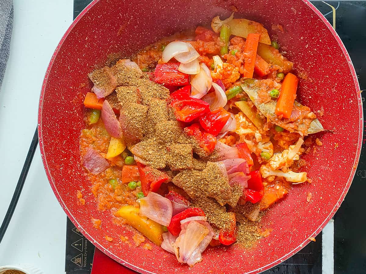 Kadai masala added to vegetable gravy in a pink wok pan.