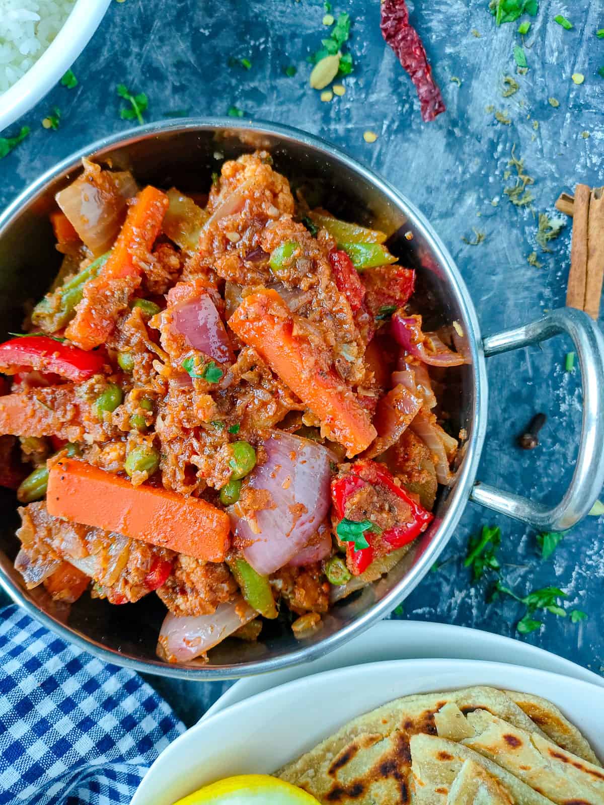 Veg kadai in a metal kadai with a bowl of rice and chapathis on a plate.