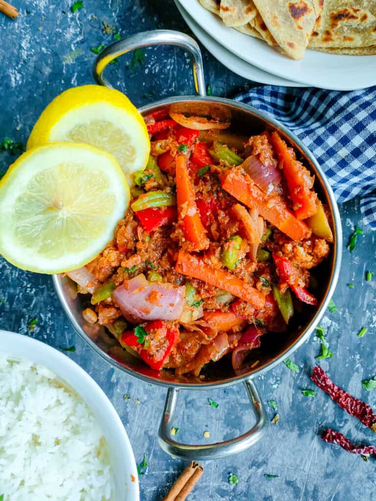 Vegetable kadai in a metal kadai with a bowl of rice and rotis on a plate.