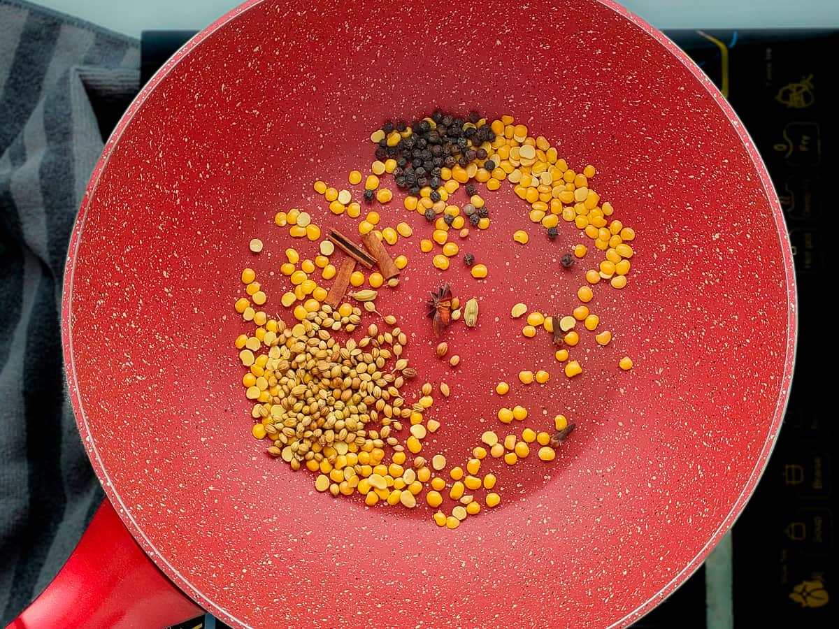 Roasted dal with whole spices in a pink wok pan.