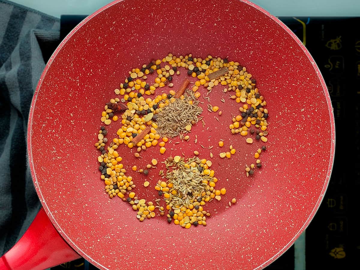 Roasted dal and whole spices with cumin and fennel seeds in a pink wok pan.