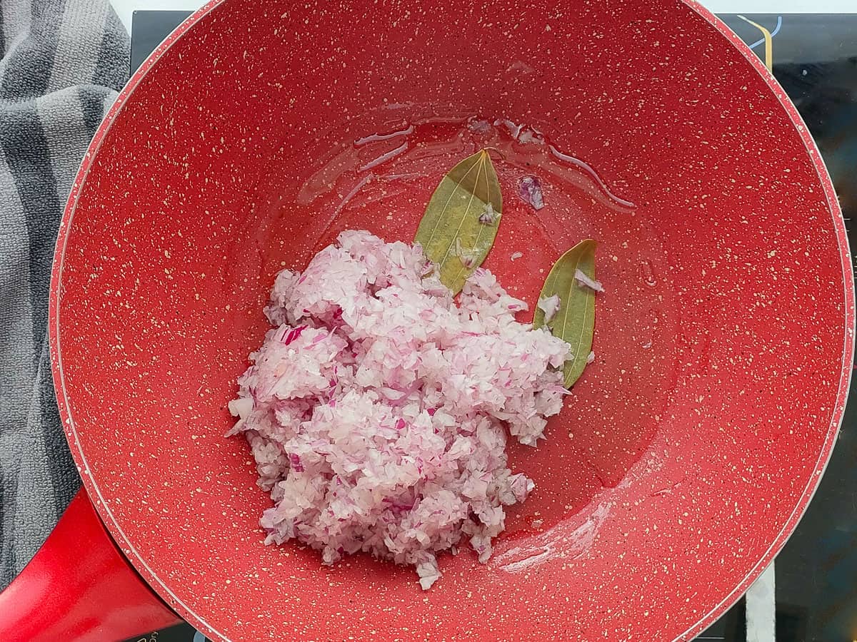 Onions and bay leaf in a pink wok pan.