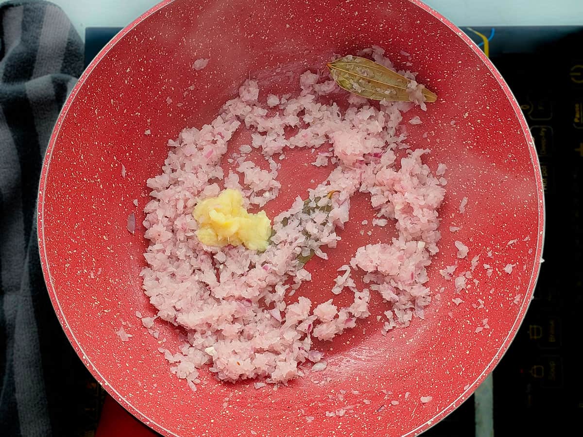 Ginger-garlic paste with onions and bay leaf in a pink wok pan.