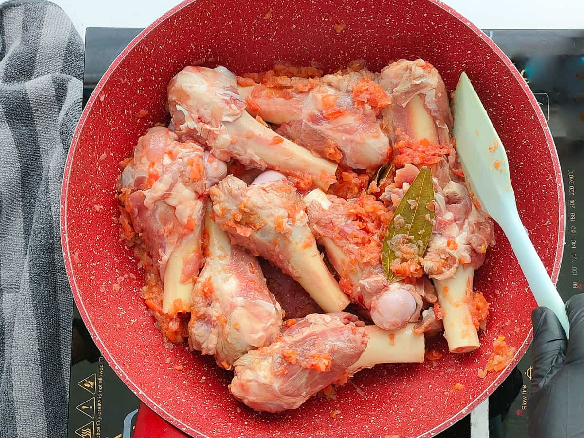 Sauteed mutton bones with onion tomato mixture in a pink wok pan.