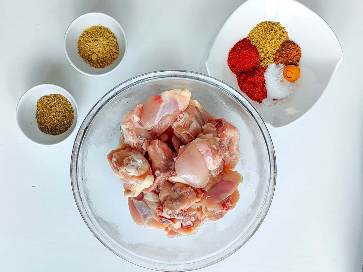 Chicken thighs and ground spices in different bowls for seasoning.