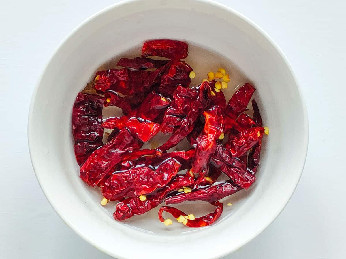 Dried red chillies soaked in water in a white bowl.