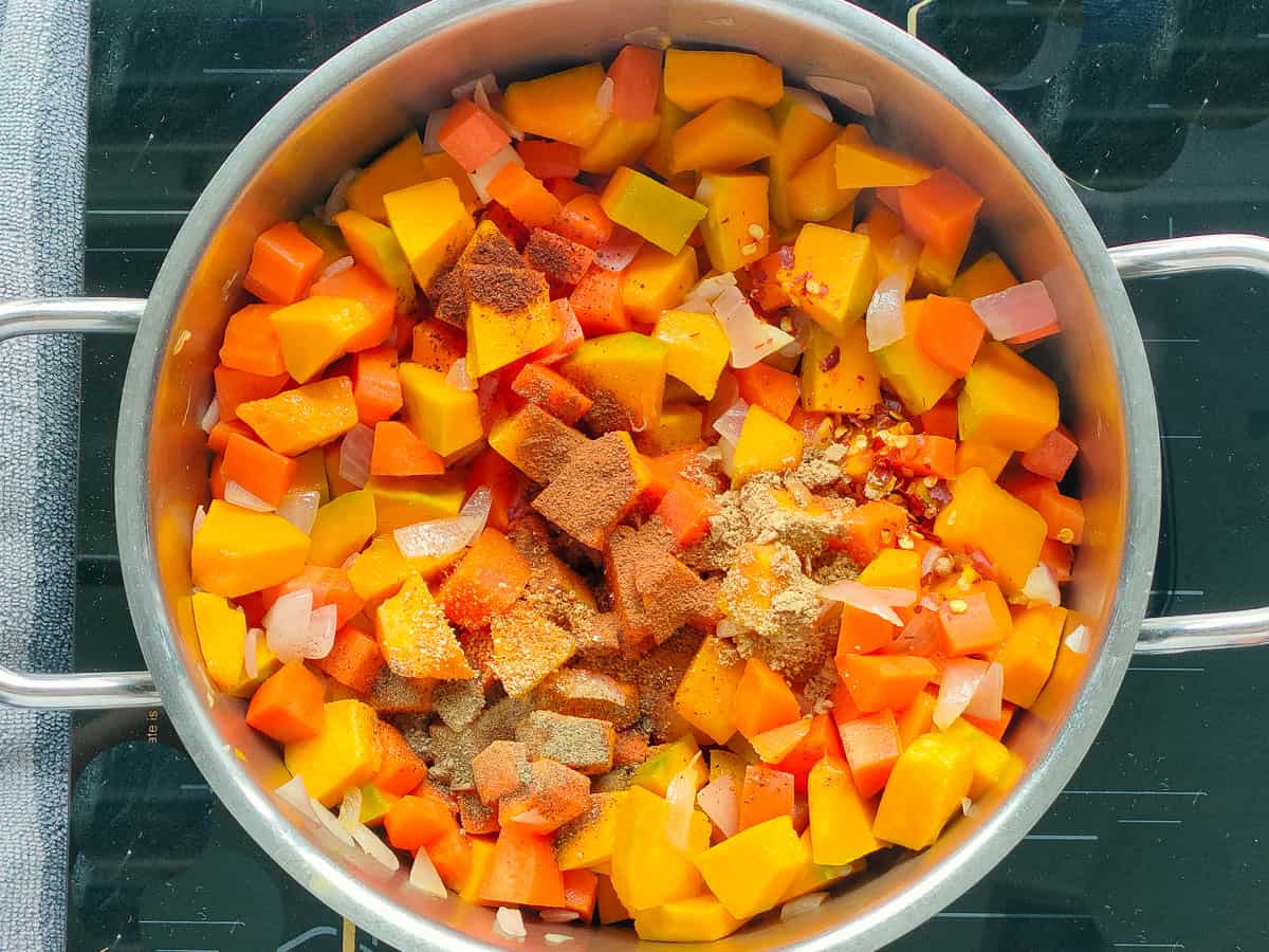 Sauteed pumpkin and carrots with spices in a large pot.