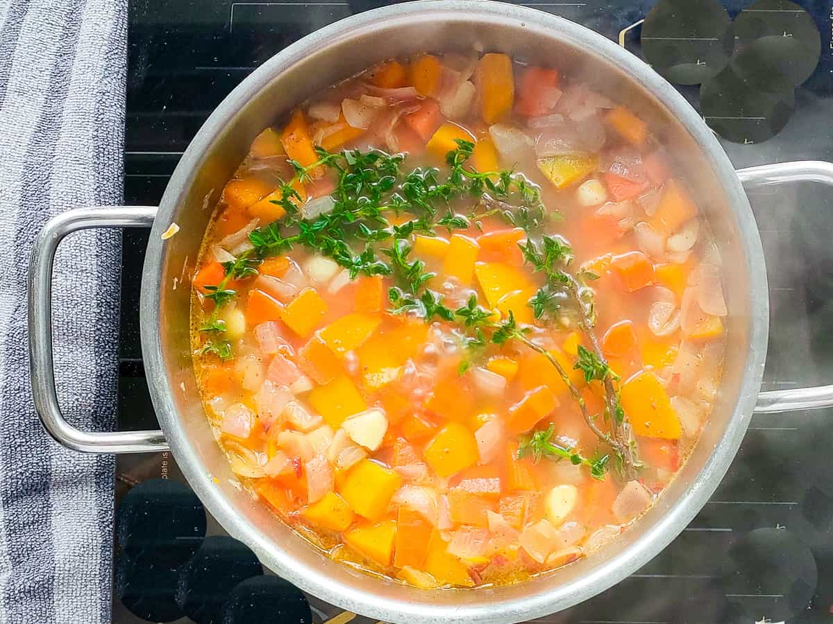 Cooked pumpkin, carrots with spices and thyme in a large pot.