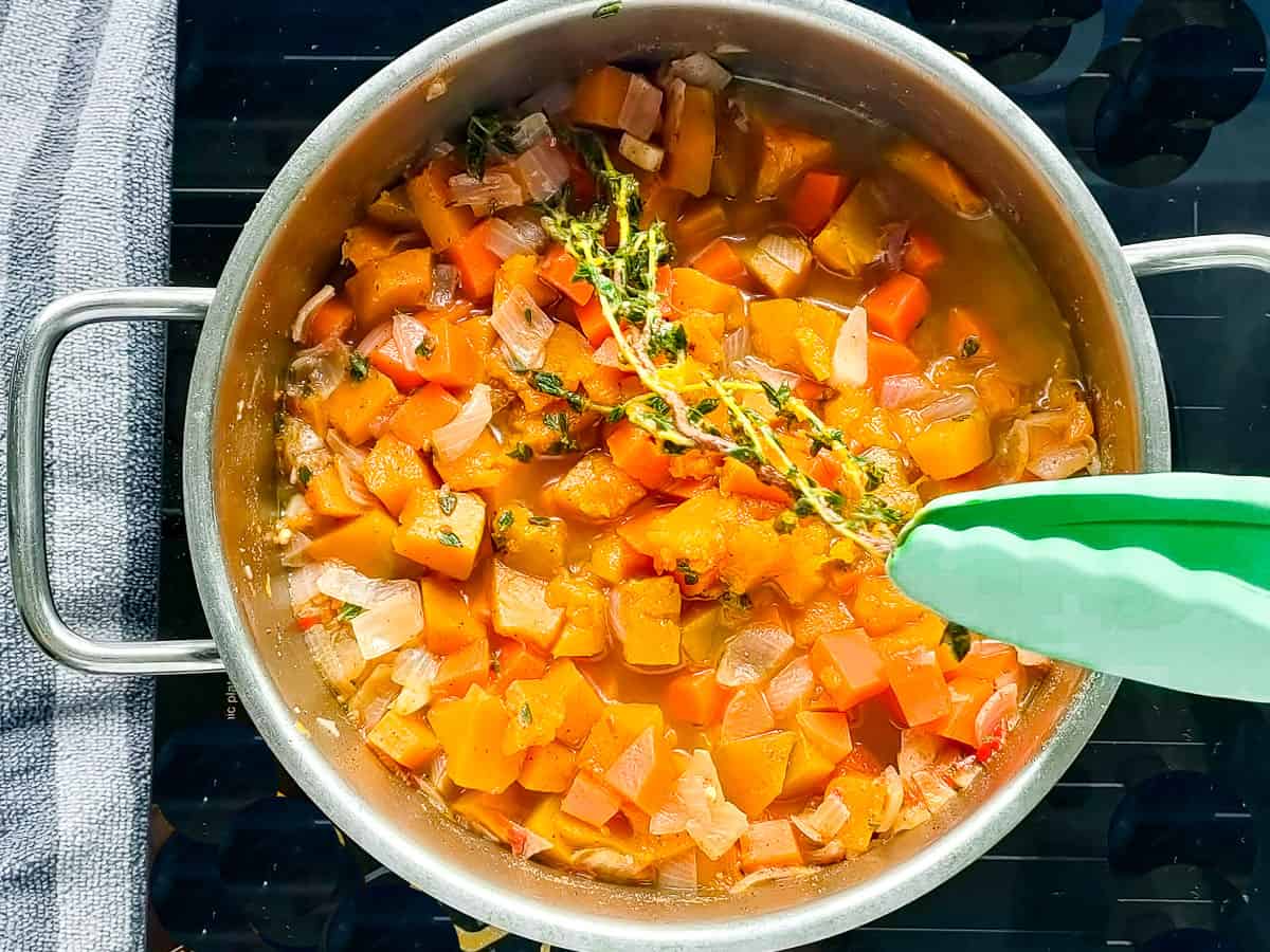 Thyme sprigs being removed from the pot of cooked vegetables.