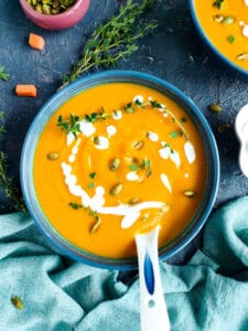 Pumpkin soup with carrots in a blue bowl and a spoon in it.