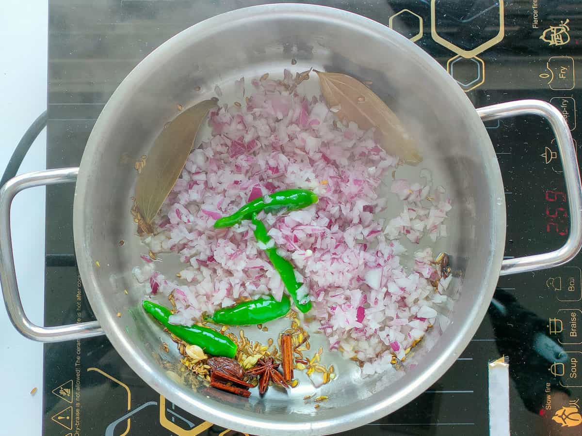 Onions and green chilies with whole spices in a large pot.