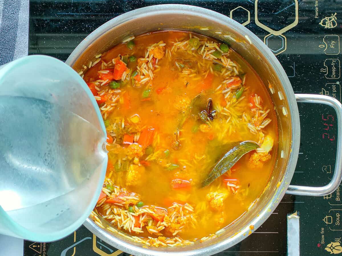 Water being added to rice and vegetables in a large pot.