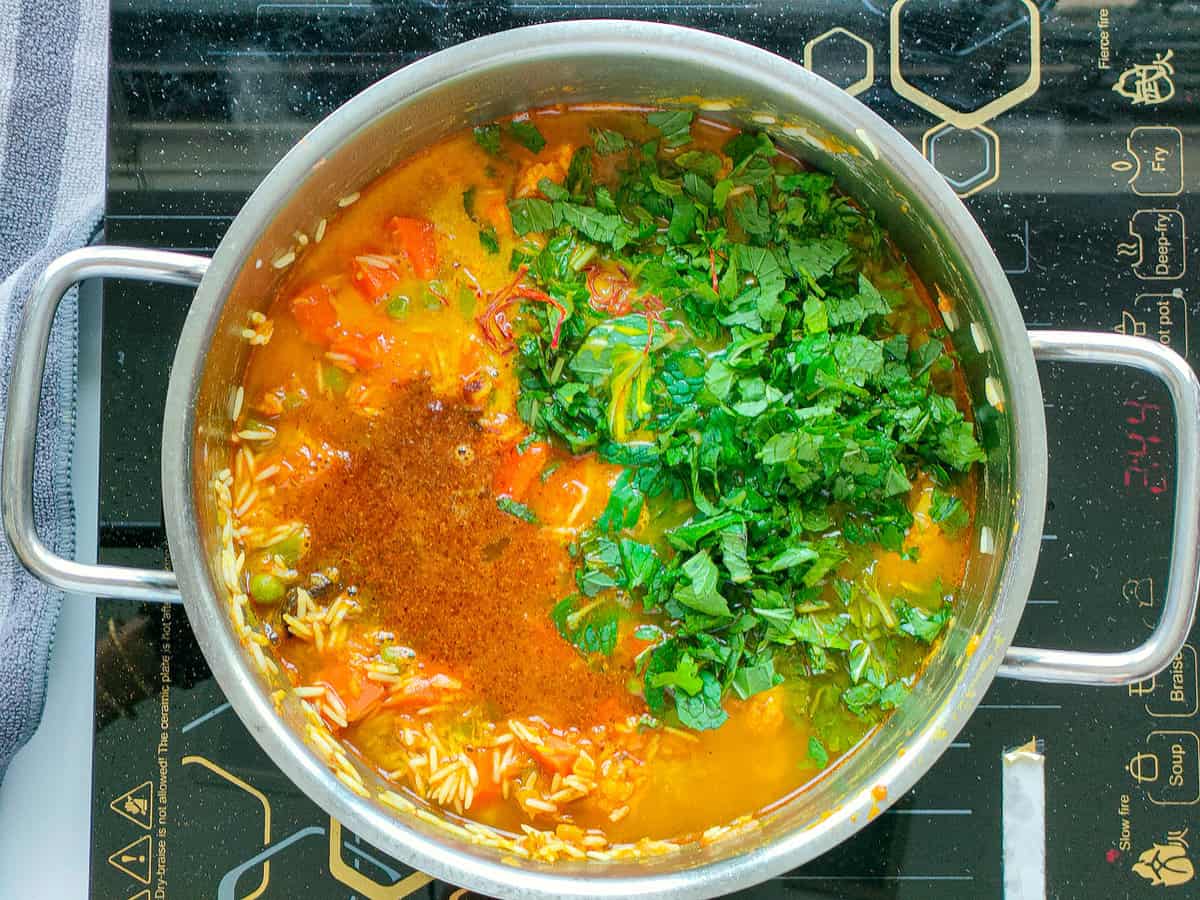 Rice and vegetables with water and herbs in a large pot.