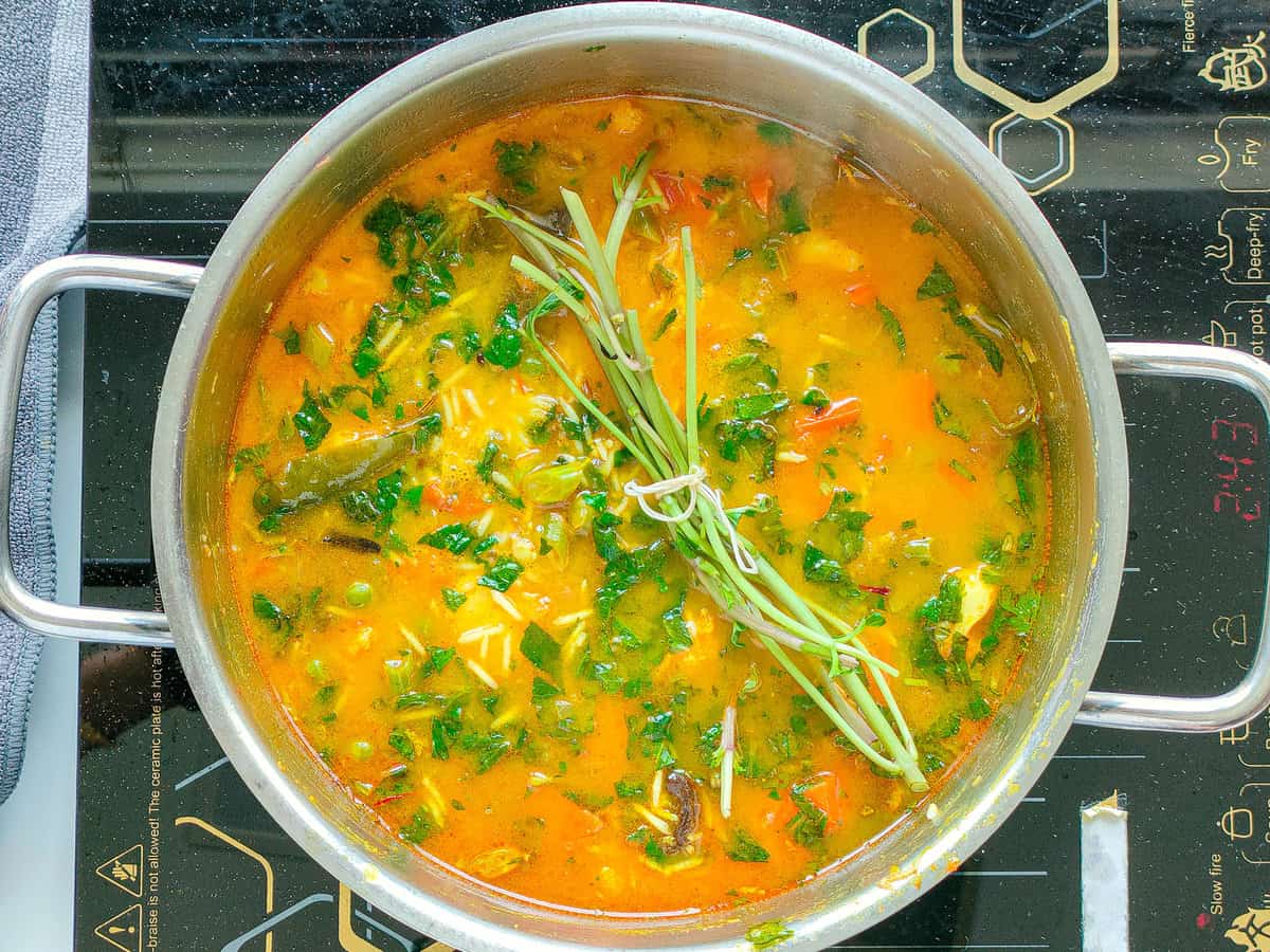 Rice and vegetables with water, herbs and mint stalks in a large pot.