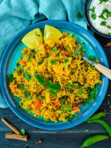 Vegetable biryani pulao on a blue plate with a spoon in it.