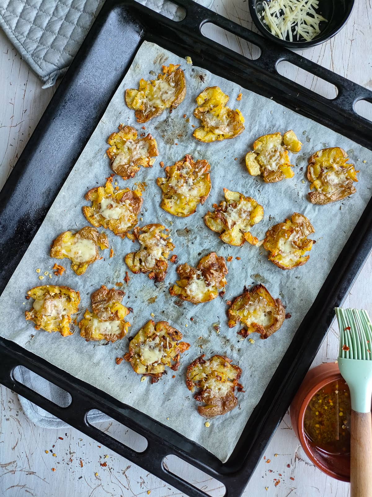 Cheesy smashed potatoes with rosemary on a sheet pan lined with parchment paper.