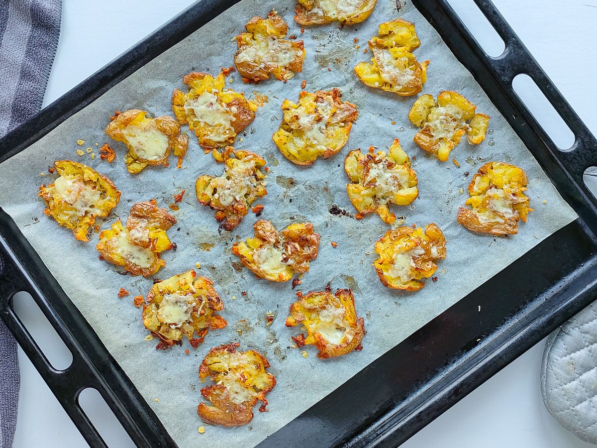 Smashed potatoes with cheese on a baking sheet.