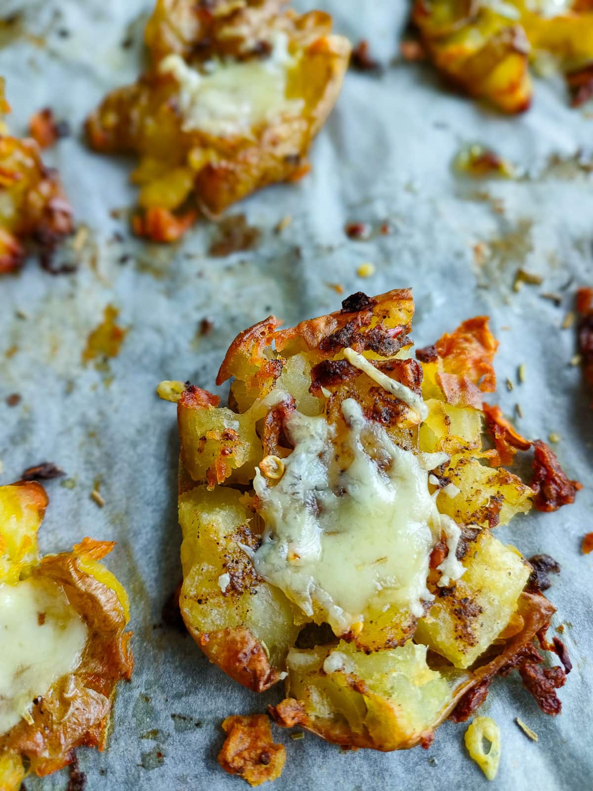 Cheesy smashed potato on a baking sheet lined with parchment paper.