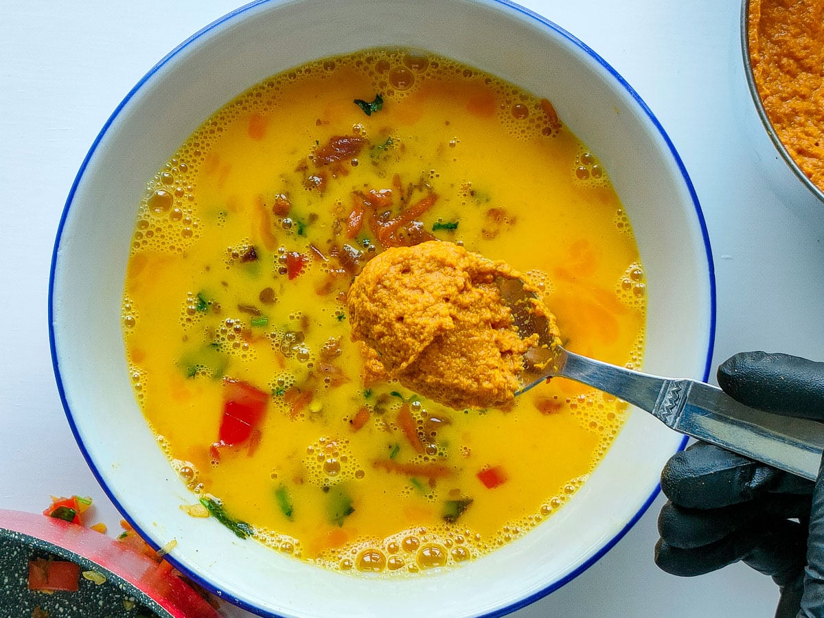 A spoon of coconut curry paste being added to beaten eggs.