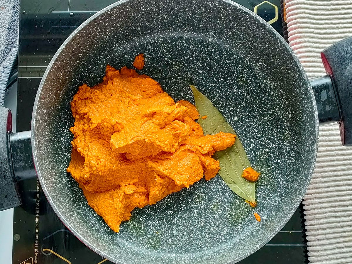 Bay leaves and coconut curry paste being sauteed in oil in a pot.