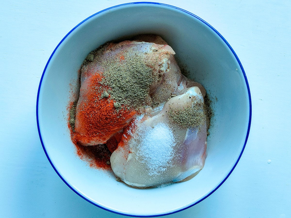 Chicken thighs with spices in a medium white bowl.