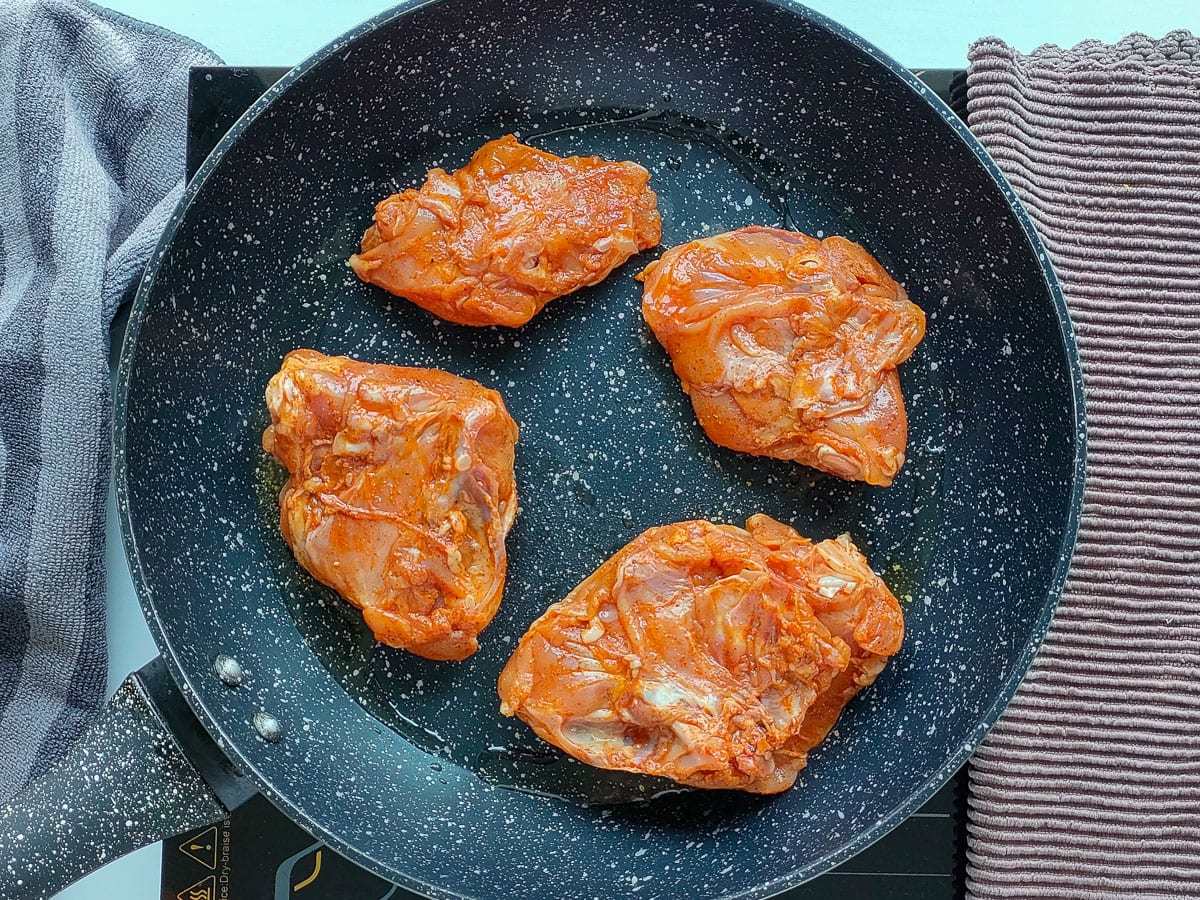 Chicken thighs being seared in a frying pan.