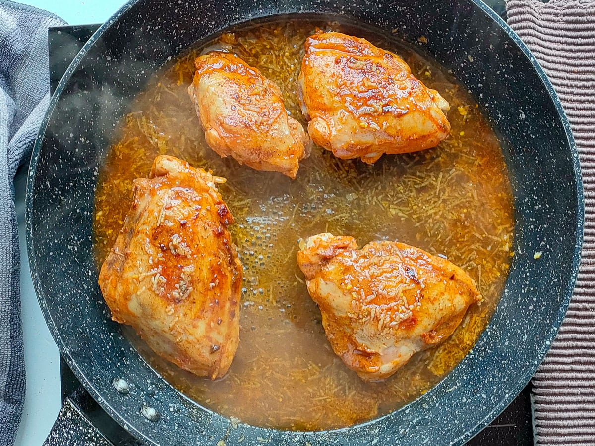 Chicken thighs with hot honey lemon pepper sauce in a frying pan.