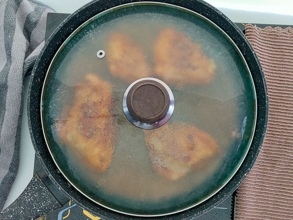 Honey garlic lemon pepper chicken thighs being cooked in a covered pan.