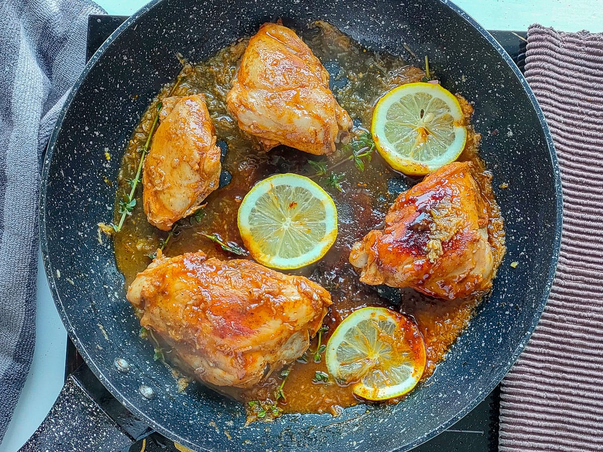 Honey lemon pepper chicken with lemon slices in a frying pan.