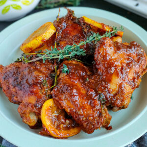 Lemon pepper honey garlic chicken thighs garnished with thyme and caramelized lemon slices on a plate.