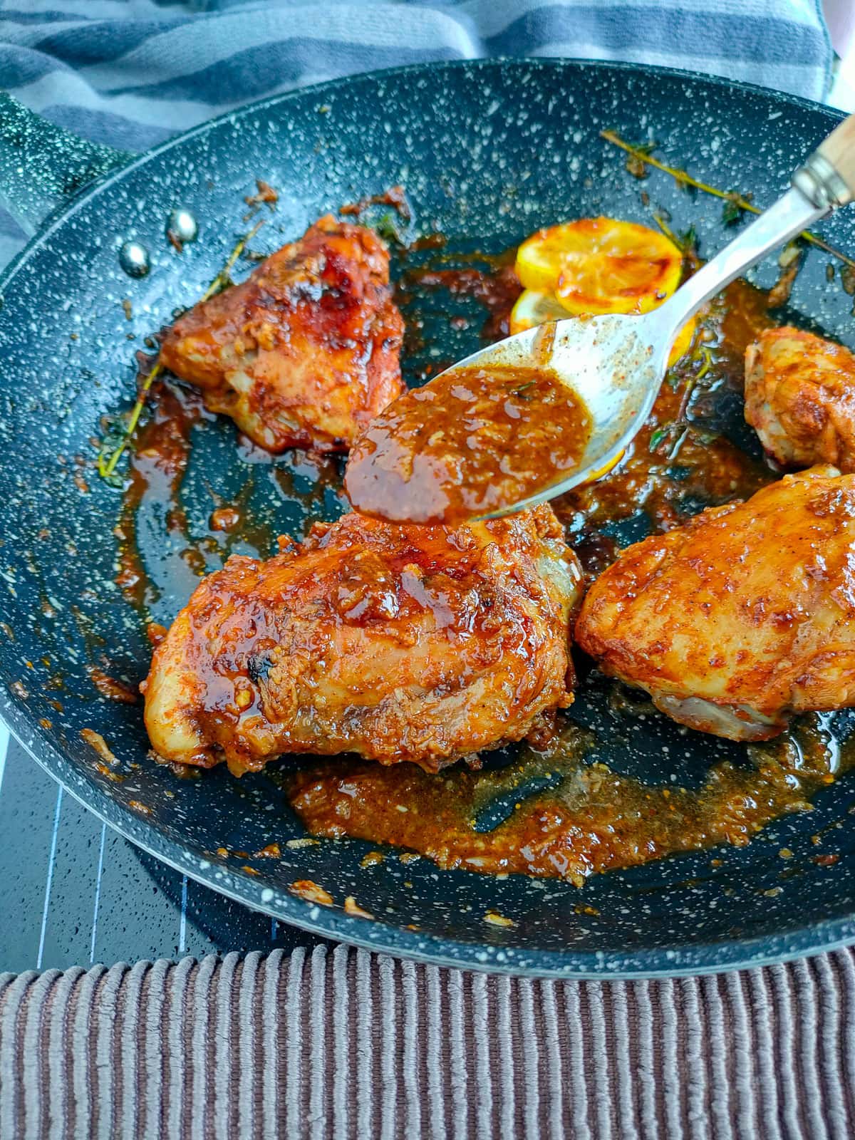 Honey garlic lemon pepper sauce being drizzled with a spoon on chicken thighs in a frying pan.