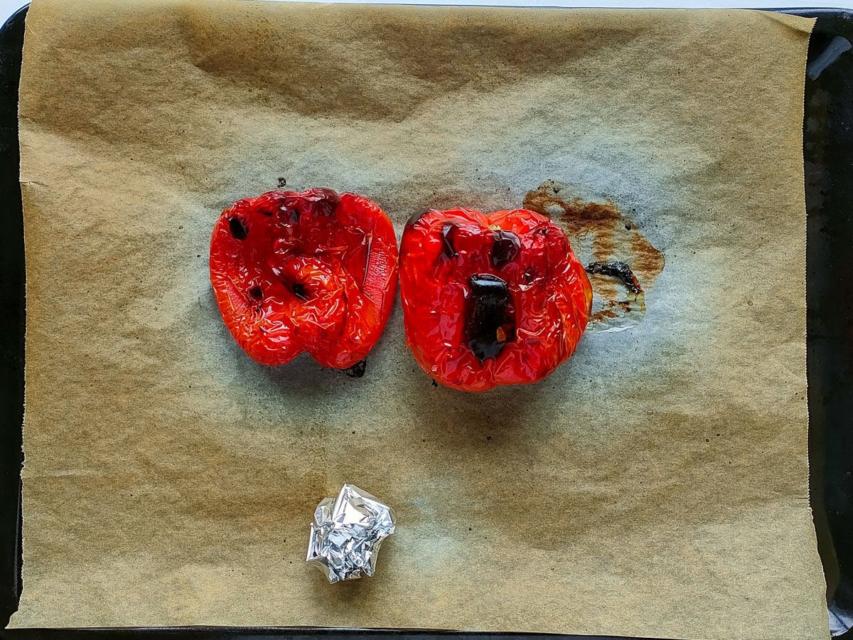 Roasted red peppers and garlic wrapped in foil on a baking tray lined with parchment paper.