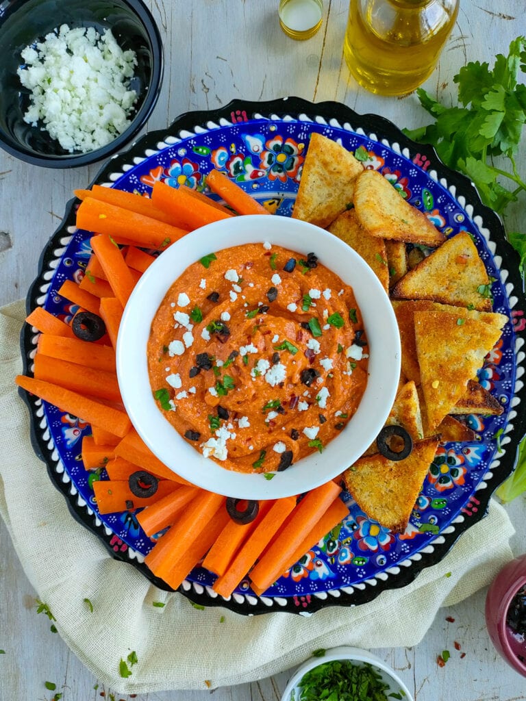 Spicy feta dip in a white bowl with carrot sticks and pita chips on a plate.