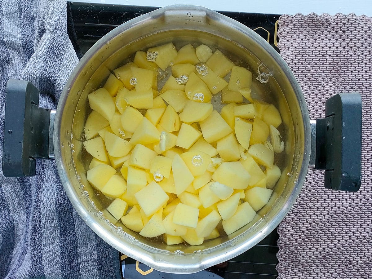 Diced potatoes with salted water and smashed garlic in a large pot.
