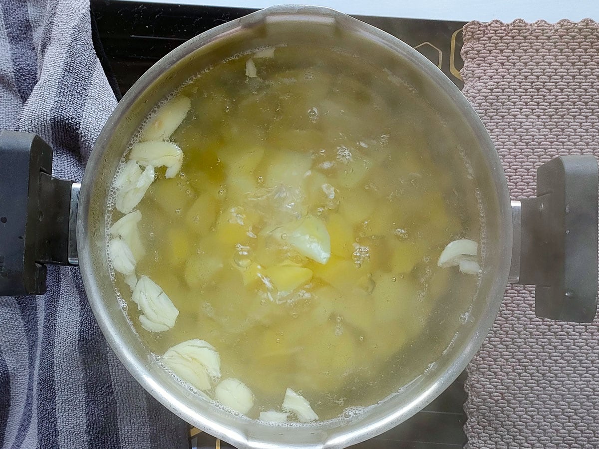 Potatoes boiling with smashed garlic in a deep pot.