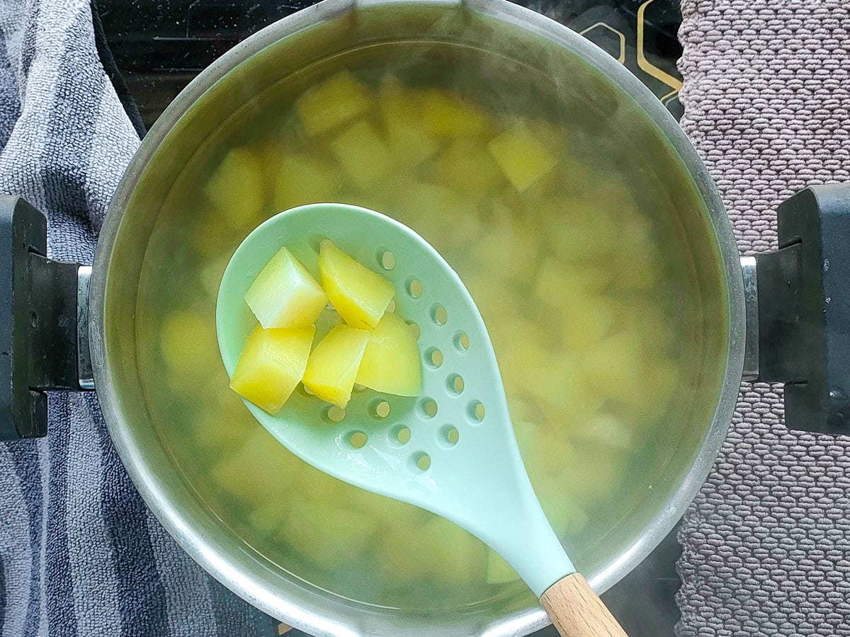 Boiled potato cubes being scooped out with a ladle from a stock pot.