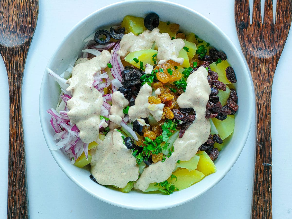 Potato salad with raisins and sugar-free dressing in a large white bowl.