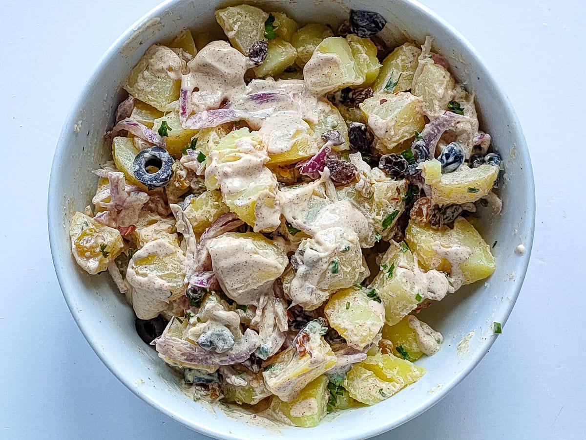 Potato salad with raisins and creamy Greek yogurt dressing in a large white bowl.