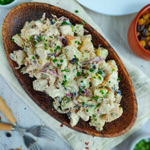 Greek yogurt potato salad with raisins on a wooden plate.