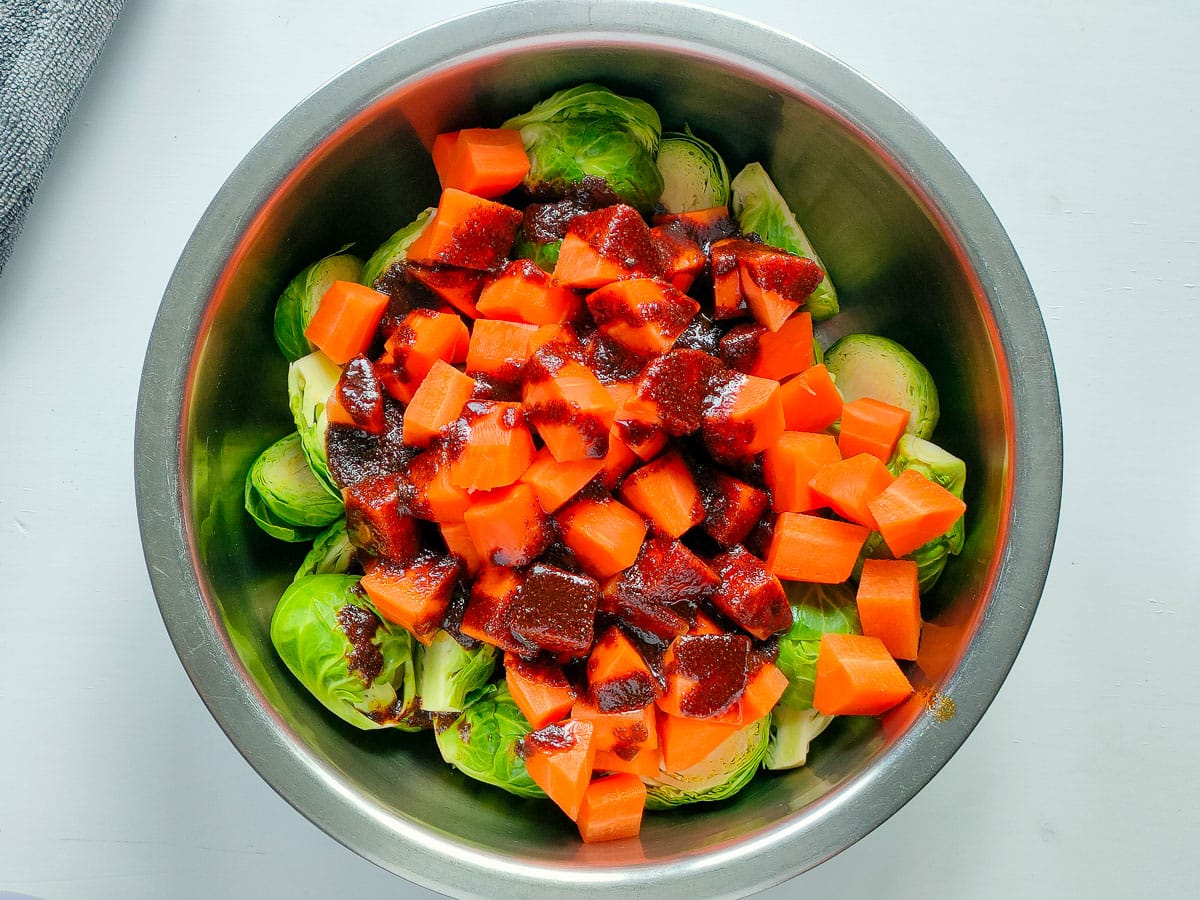 Diced carrots and brussels sprouts with balsamic seasoning in a large bowl.